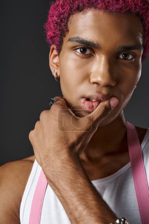 portrait of handsome stylish man with pink suspenders with hand near lips, fashion and style