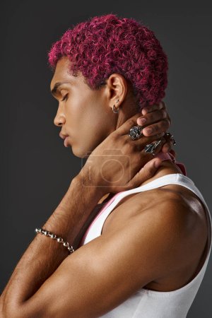 portrait of young man with pink suspenders posing in profile on gray backdrop, fashion and style