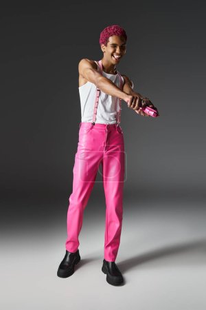 Foto de Alegre rosa peludo hombre sobresaliendo su lengua y guiño posando con rosa juguete pistola en las manos - Imagen libre de derechos