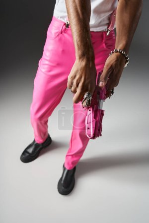 Ausgeschnittene Ansicht eines afrikanisch-amerikanischen männlichen Modells in pinkfarbenen Hosen mit Hosenträgern, die mit Spielzeugpistole posieren