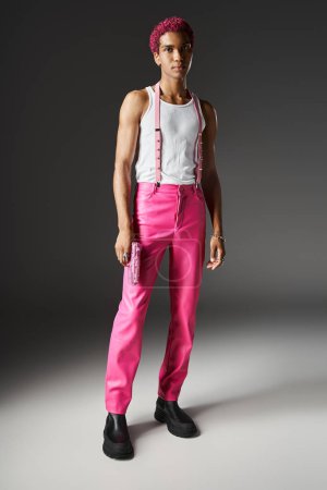 Photo for Good looking young man in pink pants with suspenders posing with toy gun and looking at camera - Royalty Free Image