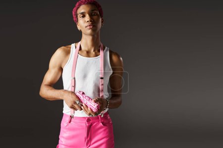 bel homme afro-américain en tenue vibrante avec bretelles et accessoires posant avec pistolet jouet
