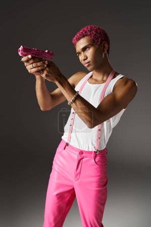 hombre elegante guapo en pantalones de color rosa con tirantes con accesorios de plata con el objetivo de su pistola de juguete rosa