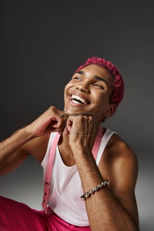 schöner stylischer Mann mit rosa Haaren, die Hände unter dem Kinn haltend und aufrichtig lächelnd, Modekonzept