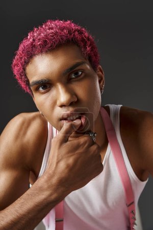 portrait de l'homme aux cheveux roses élégant avec la main sur le visage et la lèvre en regardant la caméra, concept de mode