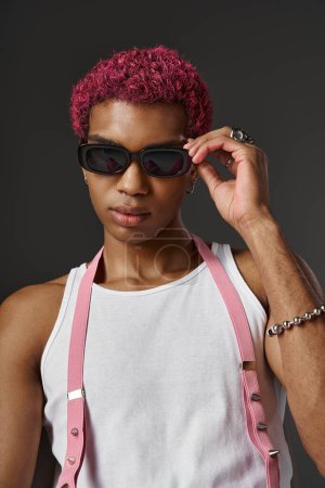 good looking man with sunglasses and silver accessories posing on gray backdrop, fashion concept