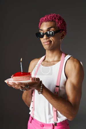 hombre afroamericano guapo en gafas de sol posando con pastel y vela ardiente, concepto de moda
