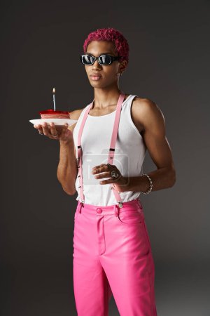 Foto de Hombre guapo en gafas de sol posando con delicioso pastel y tirantes conmovedores, concepto de moda - Imagen libre de derechos