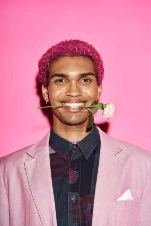 portrait of joyful young man with white rose in mouth smiling at camera and acting like doll
