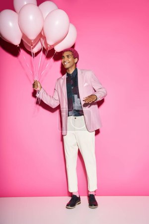 schöner junger Mann mit rosa Haaren posiert mit rosa Luftballons, die unnatürlich gestikulieren und sich wie Puppen verhalten