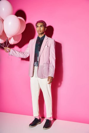 stylisches rosafarbenes männliches Model, das unnatürlich mit Luftballons in den Händen steht und wegschaut, puppenhaft
