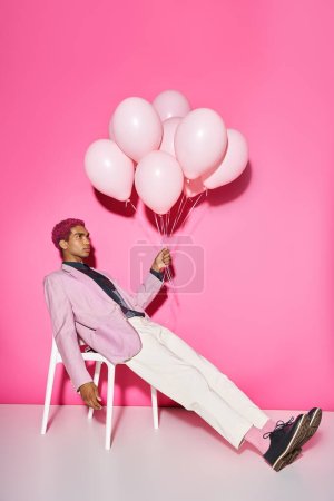 schöne junge männliche Modell posiert unnatürlich mit Luftballons in der Hand auf rosa Hintergrund, puppenhaft