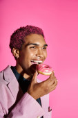 cheerful young african american man in pink blazer and earrings enjoying his donut on pink backdrop puzzle #677105790