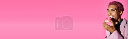 Photo for Joyous young man with curly hair and earrings enjoying donut posing on pink background, banner - Royalty Free Image