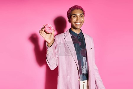 joyous man in vibrant outfit smiling unnaturally at camera and holding donut on pink backdrop