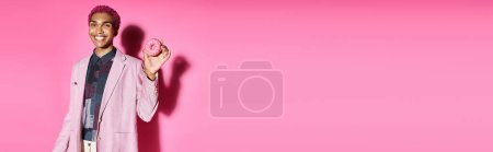 fröhlicher Mann in lebendiger Kleidung, der unnatürlich in die Kamera lächelt und Donut auf rosa Hintergrund hält, Banner