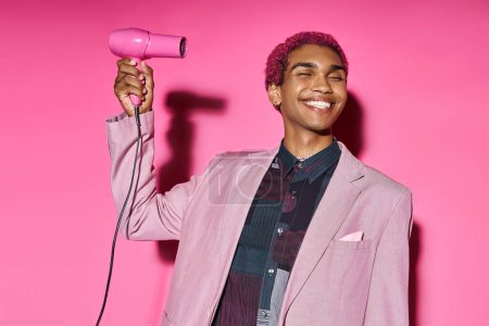 good looking stylish man in bold attire smiling weirdly with closed eyes and hairdryer in hands