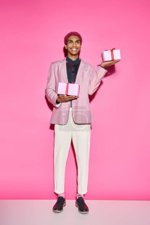 handsome african american man in vibrant outfit posing with presents in hands on pink backdrop
