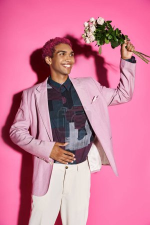 fröhlicher junger Mann im rosafarbenen Blazer posiert wie eine Puppe mit Rosenstrauß in den Händen und schaut weg