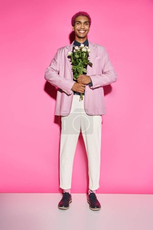 hombre guapo con el pelo rizado posando de forma antinatural y sonriendo con ramo de rosas delante de él