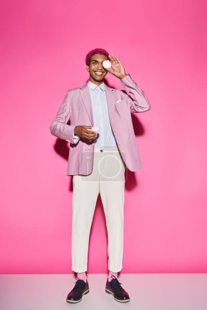 Foto de Hombre guapo sonriendo antinaturalmente y de pie quieto con zefir en las manos sobre el telón de fondo rosa - Imagen libre de derechos