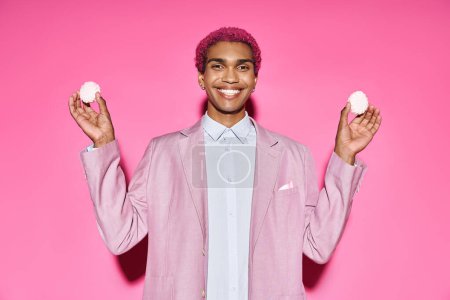 guapo joven modelo masculino sonriendo antinaturalmente y sosteniendo delicioso zefir en las manos en rosa telón de fondo