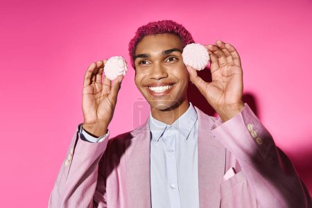 fröhlicher Mann posiert mit köstlichem rosa Zefir in Gesichtsnähe auf rosa Hintergrund und verhält sich wie eine männliche Puppe