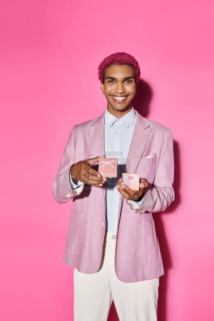 fröhlicher junger Mann posiert unnatürlich mit Geschenk in den Händen lächelnd in die Kamera auf rosa Hintergrund