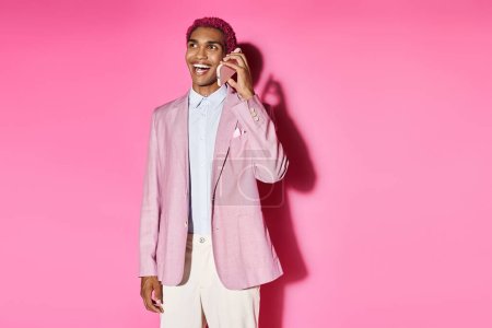 junger stilvoller Mann, der unnatürlich fröhlich lächelt und auf rosa Hintergrund telefoniert