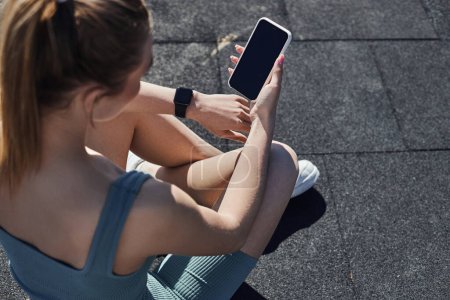 top view of fit woman in activewear with fitness tracker on wrist using smartphone after workout