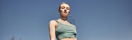 blonde and fit woman in grey crop top standing and looking at camera after workout, banner