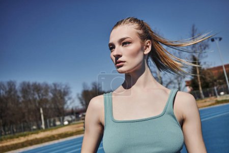 Porträt einer blonden jungen Sportlerin im grauen Crop Top, die nach dem Training im Freien wegschaut
