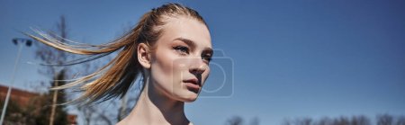 portrait of blonde young sportswoman with ponytail looking away after working out outdoors, banner