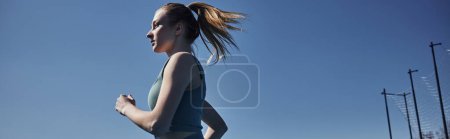 Foto de Vista lateral de mujer en forma rubia en ropa deportiva corriendo al aire libre, motivación y banner deportivo - Imagen libre de derechos