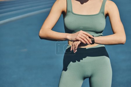 Foto de Deportista recortada en ropa deportiva de pie y comprobando su rastreador de fitness en pista de jogging - Imagen libre de derechos