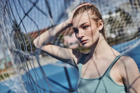 Photo for Portrait of blonde and fit woman standing in activewear near net after working out outdoors - Royalty Free Image