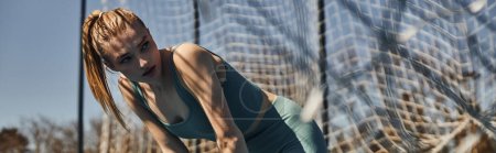 Photo for Sporty young woman with ponytail in sportswear resting while working out outdoors near net, banner - Royalty Free Image