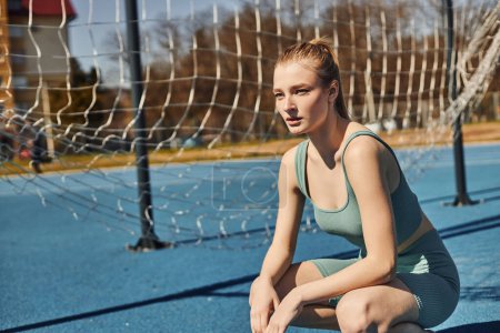 tired young woman with ponytail in activewear resting while sitting on haunches after workout