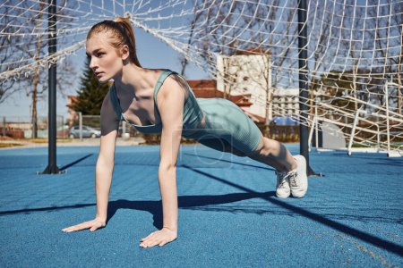 pretty young sportswoman with ponytail exercising in activewear near net outdoors, doing press ups