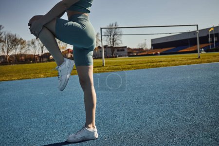 Téléchargez les photos : Vue recadrée d'une sportive flexible faisant de l'exercice en vêtements de sport serrés à l'extérieur, jambes tendues - en image libre de droit