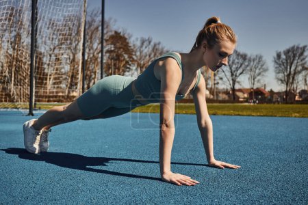 young sportswoman with ponytail exercising in activewear near net outdoors, doing press ups