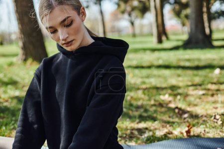 portrait of sportive young woman in black hoodie exercising in green park, nature and sport