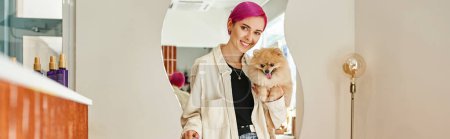 stylish woman with pomeranian spitz smiling at camera near reception desk in dog hotel, banner