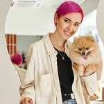 stylish woman with pomeranian spitz smiling at camera near reception desk in dog hotel, banner