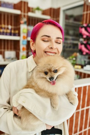 joyful woman with closed eyes embracing loveable pomeranian spitz in dog hotel, pet-friendly concept