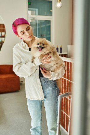 woman with purple hair holding and hugging pampered pomeranian spitz near reception in pet hotel