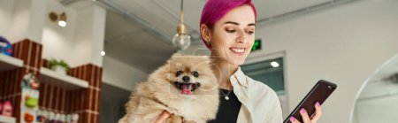 Photo for Happy woman with funny pomeranian spits looking at smartphone in lobby of pet hotel, banner - Royalty Free Image