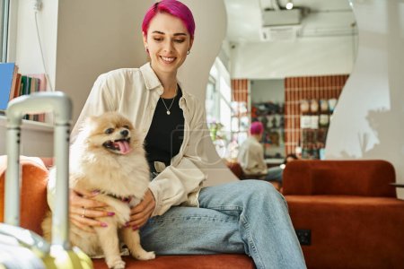 zufriedene Frau sitzt neben Reisetasche im Haustierhotel und kuschelt lustigen Hund, Haustier-Unterkunft