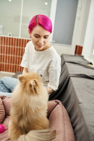 Foto de Sonriente trabajador del hotel de mascotas mirando perrito esponjoso en acogedor hotel de mascotas, cuidado y afecto - Imagen libre de derechos