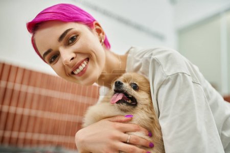 fröhliche lila-haarige Frau umarmt entzückende Hündin in Haustier-Hotel, Zuneigung von Haustier ein Hundesitter